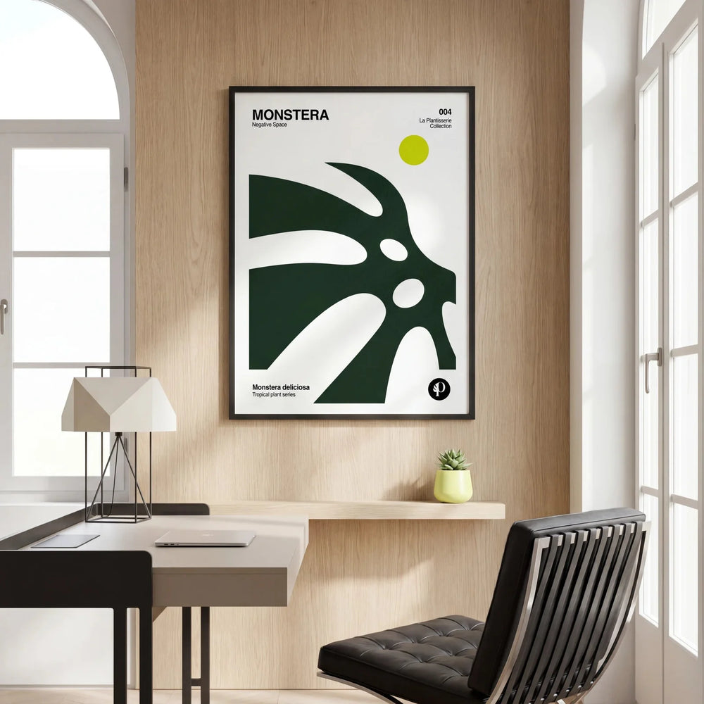 Lámina de Monstera Tropical Series enmarcada en negro sobre un escritorio de madera con silla de cuero negra