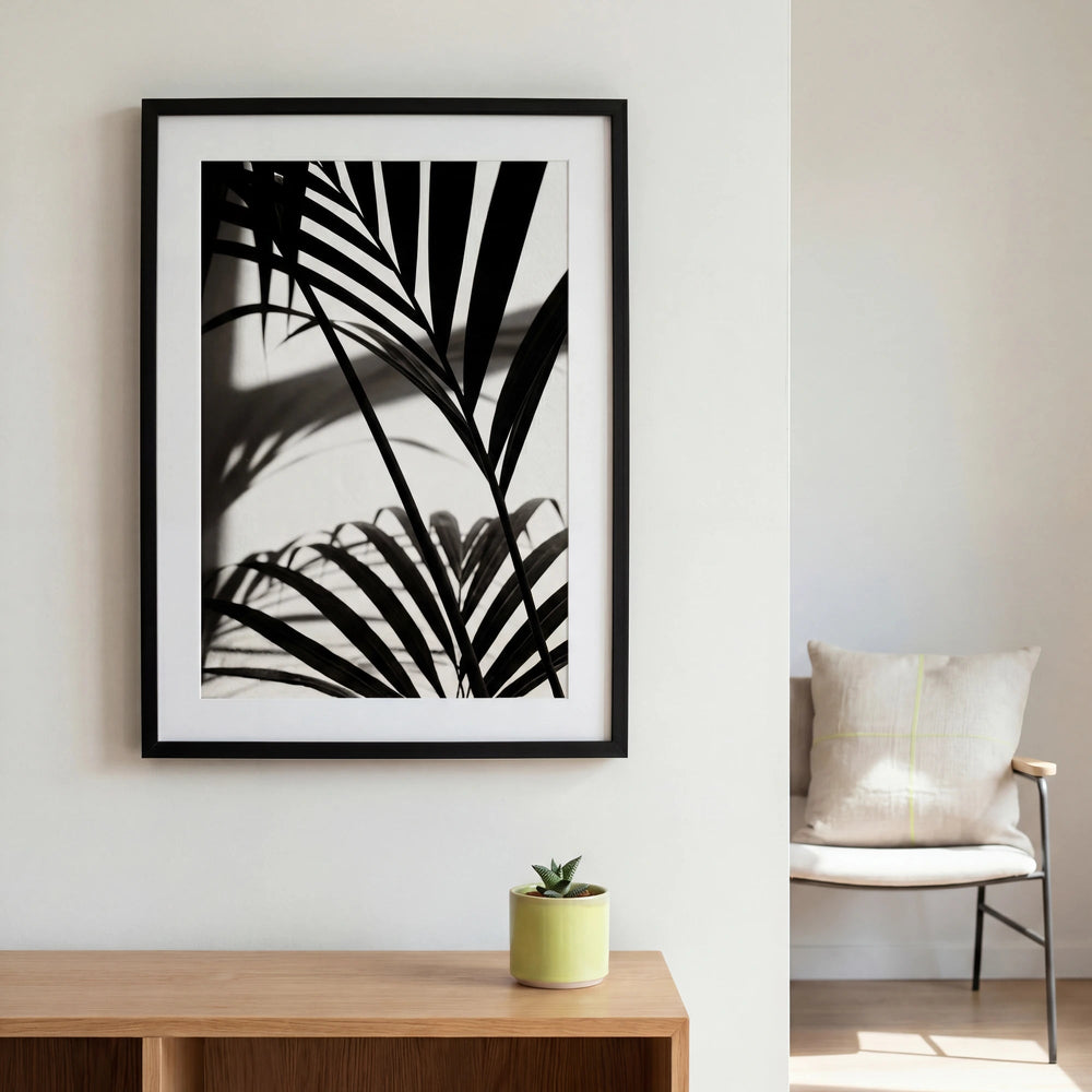 Lámina de palmera Kentia en blanco y negro enmarcada sobre una consola de madera con una pequeña planta